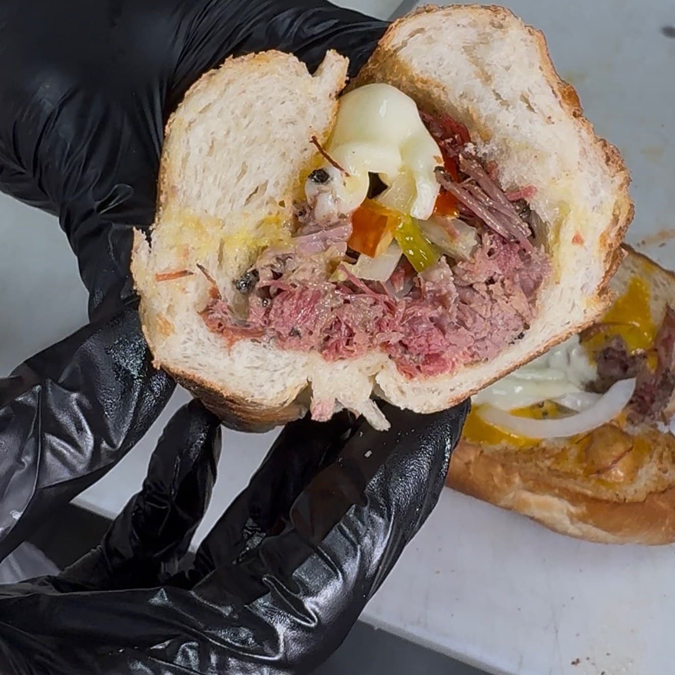 Hoagie House Brisket Sandwich — a halved hoagie showing smoked brisket, melted provolone, sweet peppers, and onions on a crusty roll